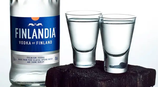 Butelka wódki Finlandia i dwa kieliszki z wódką na ciemnym tle.