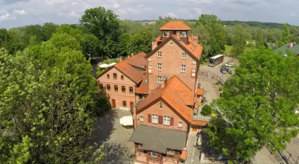 Hotel Młyn Elbląg, ceglane budynki z czerwonymi dachami, otoczone zielenią.