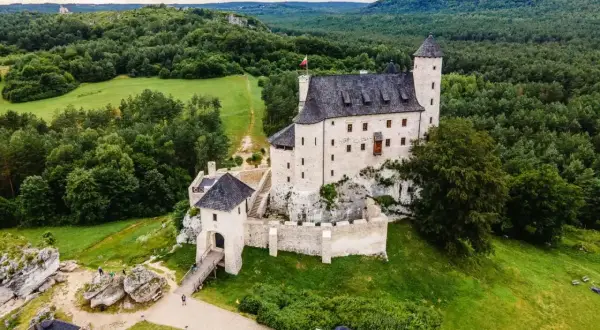 Malowniczy zamek Bobolice, wzniesiony na skale, otoczony zielonymi lasami i polami.
