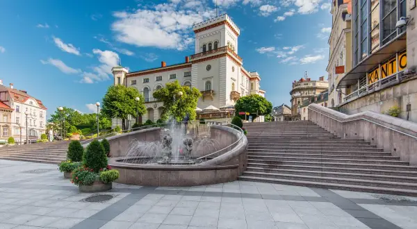 Słoneczny rynek w Bielsku-Białej z fontanną i schodami prowadzącymi do zabytkowych budynków.