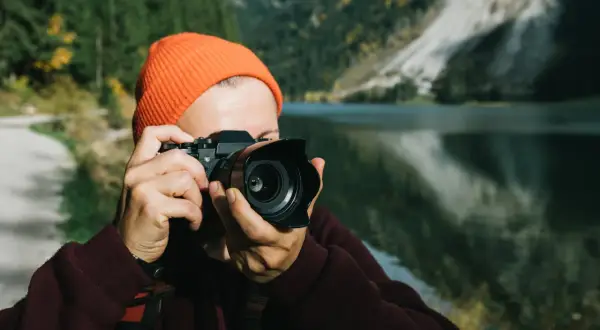 Osoba w pomarańczowej czapce robi zdjęcie aparatem, który mógłby być Nikon D7000. Dane techniczne tego modelu pozwalają na uchwycenie piękna górskiego krajobrazu.