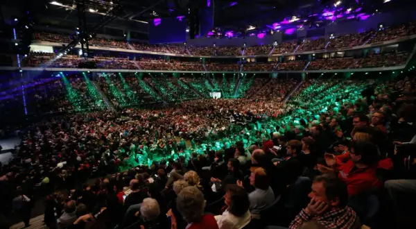 Tausende Menschen in einer Arena, beleuchtet von grünen und violetten Lichtern. Eine beeindruckende Kulisse für eine mega church Veranstaltung.