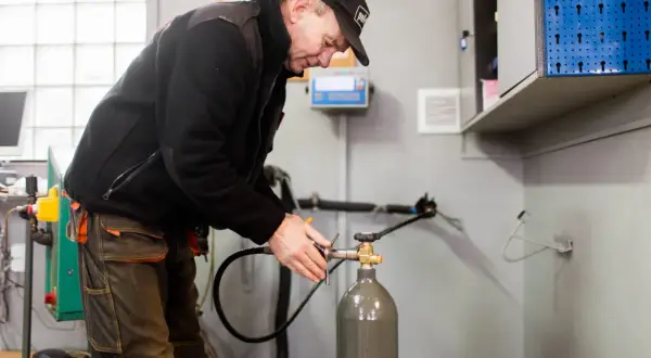 Pracownik w czapce i roboczych spodniach dokonuje napełniania butli CO2, podłączając wąż do zaworu.
