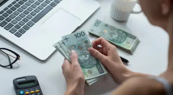 Dłonie liczą banknoty 100 zł. Obok leży laptop, kalkulator i okulary. To kwota wolna od zajęcia, którą można przeznaczyć na bieżące wydatki.
