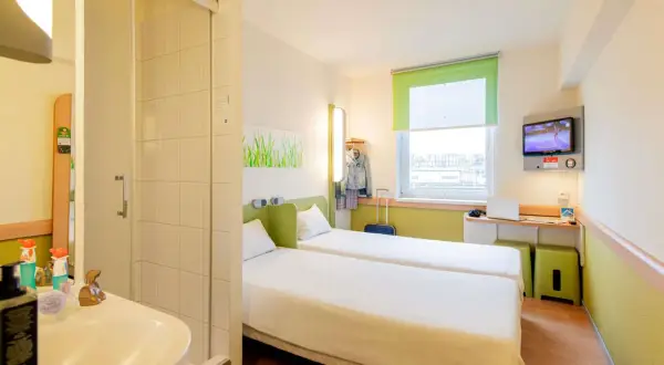 Pokój w hotelu Ibis z dwoma łóżkami, łazienką, biurkiem z laptopem i telewizorem.