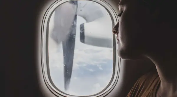 Frau blickt aus dem Flugzeugfenster, während das Flugzeug turbulenzen extrem durchfliegt. Wolken und ein Propeller sind sichtbar.