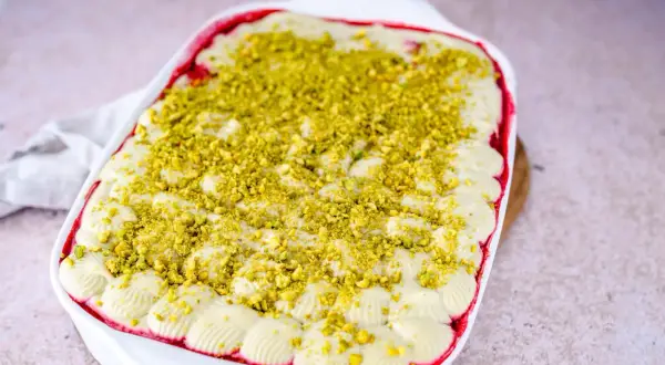 Ein cremiges Pistazien Tiramisu in einer weißen Auflaufform, bestreut mit gehackten Pistazien.