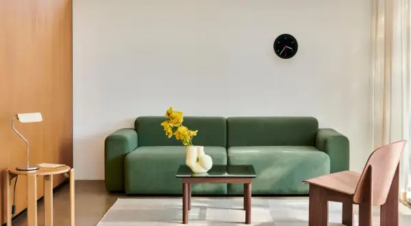 Grünes Sofa, Holzsessel und Beistelltisch im skandinavischen Einrichtungsstil. Gelbe Blumen in einer Vase auf dem Couchtisch.