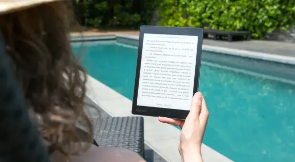 Une personne lit un epub en ligne au bord d'une piscine, profitant du soleil et d'une lecture immersive.