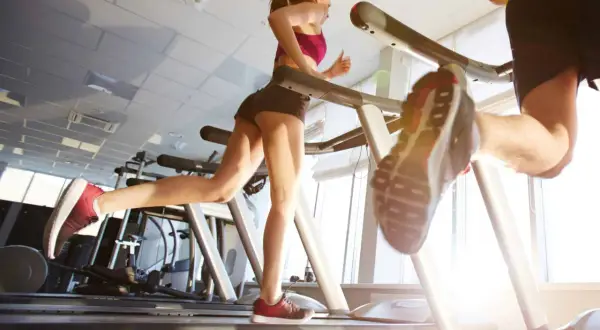 Due persone corrono sui tapis roulant in palestra. Nonostante correre fa venire la cellulite, loro si allenano con determinazione.