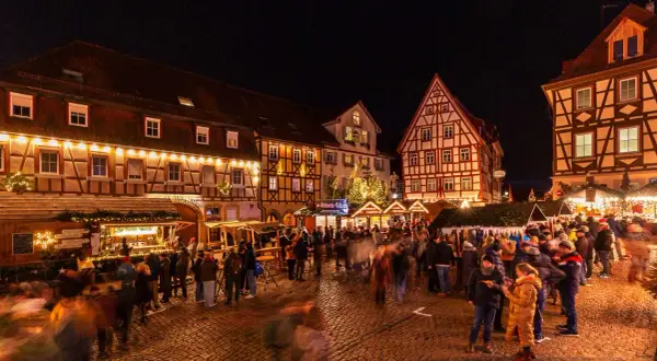 Bunte Lichter und geschäftiges Treiben auf dem **Bad Wimpfen Weihnachtsmarkt**. Fachwerkhäuser und Buden laden zum Verweilen ein.