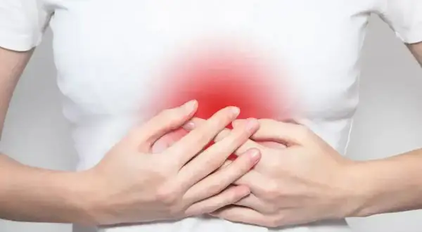 Dłonie obejmujące brzuch, gdzie czerwony obszar symbolizuje ból w splocie słonecznym.
