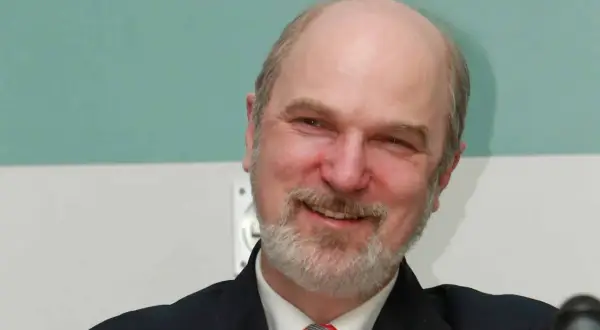 Ein Mann mit Glatze und Bart, Thomas Schirrmacher, lächelt in die Kamera. Er trägt einen dunklen Anzug und eine Krawatte.