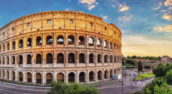 Colosseum i Rom, en ikonisk gammal stad i Italien, badar i gyllene solljus. Turister promenerar på torget framför den imponerande amfiteatern.