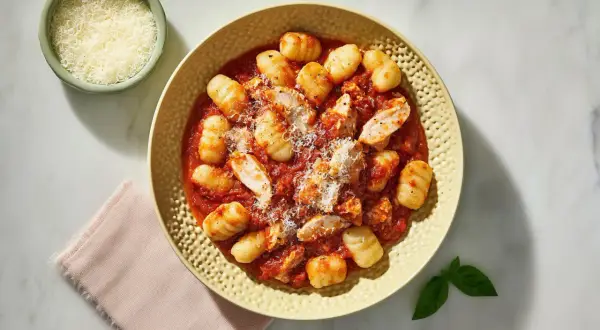 Pyszne gnocchi z kurczakiem w sosie pomidorowym, posypane parmezanem.