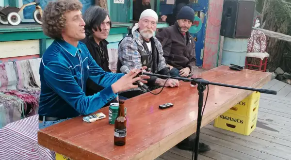 Hombres sentados en una mesa de madera en el bar de Joe Cabo de Gata, con micrófonos y botellas de cerveza.