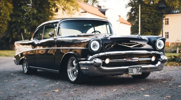 Svart Chevrolet Bel Air bil från 1957 parkerad på grusväg med höstlöv.