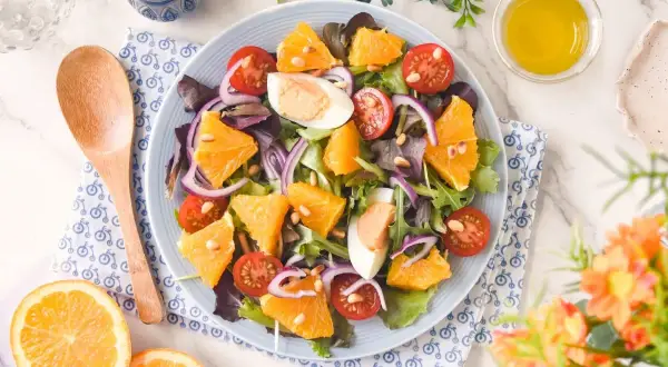 Ensalada de naranja vibrante con tomates cherry, huevo duro, cebolla morada y piñones. Una delicia fresca y colorida.