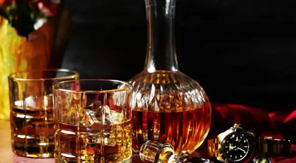 Elegancka karafka i szklanki z whisky, złoty zegarek i spinki do mankietów. Zastanawiasz się, ile cukru ma whisky?