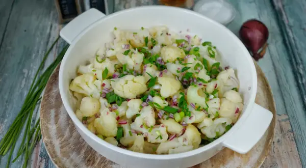 Frischer blumenkohl salat mit roten Zwiebeln und Schnittlauch, serviert in einer weißen Schüssel auf rustikalem Holz.