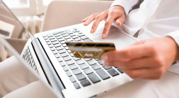 Kobieta z kartą płatniczą w dłoni wykonuje transakcję online, korzystając z laptopa. To wygodne Santander sesje.
