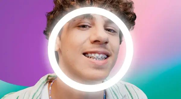 Ragazzo con cera apparecchio, sorride con un cerchio luminoso attorno al viso. Sfondo sfumato viola e verde.