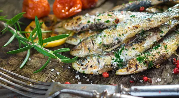 Délicieuses sardines à la plancha, parsemées d'herbes fraîches, accompagnées de tomates cerises rôties et d'une branche de romarin sur fond de bois rustique.
