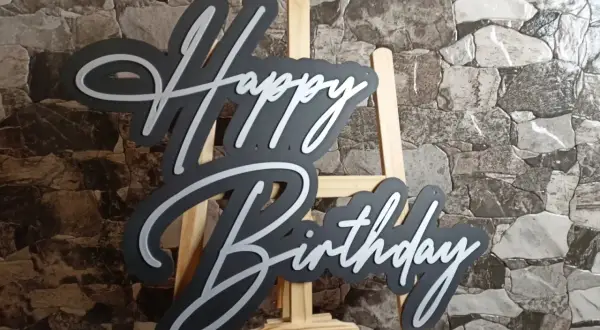 Czarny napis "Happy Birthday" z białymi obrysami, stojący na sztaludze. Idealny na życzenia "sto lat"!