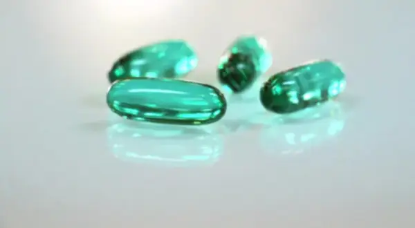 Zielone kapsułki leżą na białym tle. Czy ibuprofen jest szkodliwy? To pytanie nurtuje wiele osób.