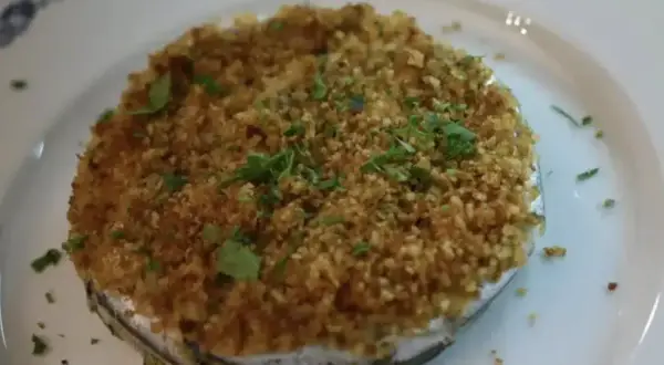 Tortino di alici dorato e croccante, guarnito con prezzemolo fresco, servito su un piatto bianco con bordo blu.