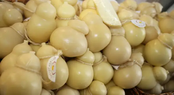 Un cesto pieno di formaggio podolico, alcuni a forma di pera, legati con spago. Un pezzo di formaggio è appoggiato sopra.