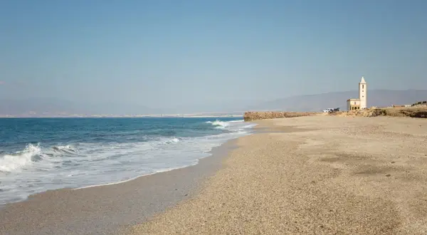 La Fabriquilla, Almería. Una playa de guijarros con el mar azul y una torre blanca solitaria.