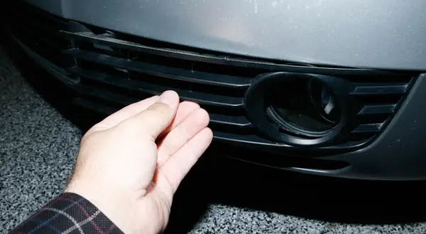 Dłoń naciska na kratkę zderzaka Audi A6 C5, obok otworu na światło przeciwmgielne.