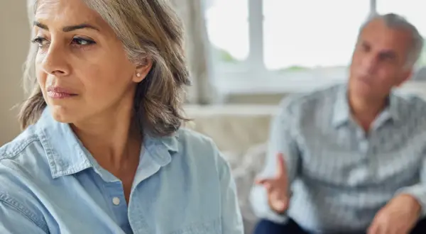 Een vrouw kijkt weg tijdens een gesprek, de man op de achtergrond gebaart. Dit beeld roept de vraag op: wanneer heeft relatietherapie geen zin?