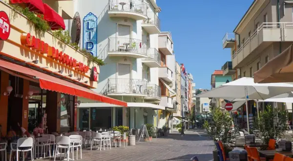 Passeggiata serale a Gabicce Mare: tavolini all'aperto di un caffè, hotel Lido e negozi colorati.