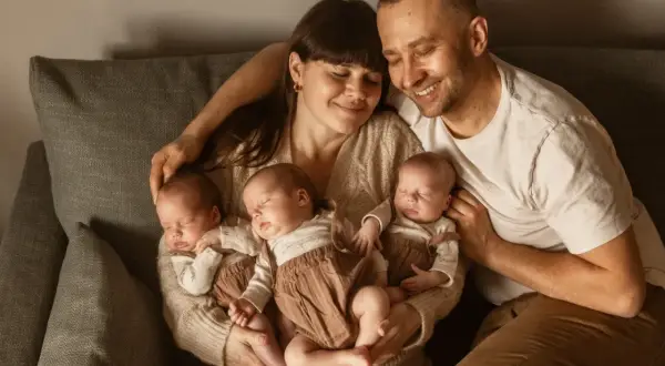 Szczęśliwa sesja noworodkowa z rodzicami tulącymi czworo śpiących dzieci.