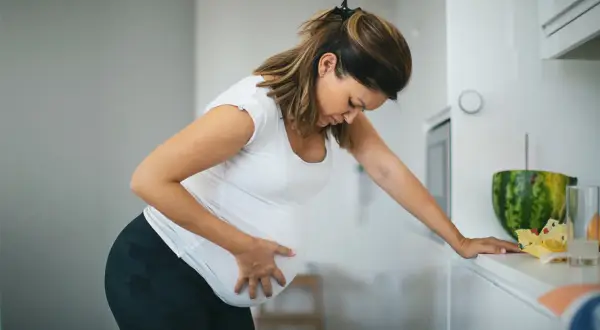 Schwangere Frau mit Hand auf dem Bauch, die sich vorbeugt. Sie fragt sich, ab wann Vorwehen auftreten können.