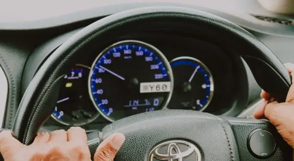 Dłonie na kierownicy, wskazówka prędkościomierza na 60 km/h. Wspomaganie kierownicy ułatwia jazdę.