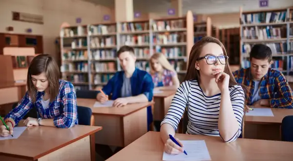 Uczniowie w bibliotece piszą test. Zastanawiają się, ile trwa szkoła zaoczna, gdy skupiają się na zadaniach.
