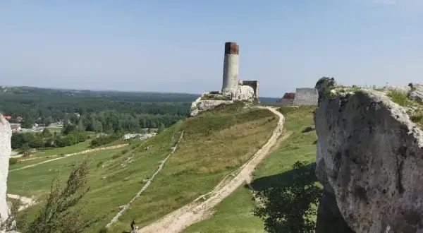 Ruiny zamku na wzgórzu, z wieżą i fragmentami murów. W dole ścieżka, idealna na rowerowe wycieczki po okolicach Częstochowy.