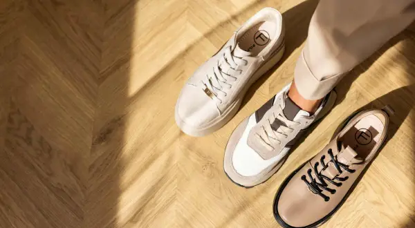 Ciekawe, jakie buty do cygaretek zimą? Na drewnianej podłodze leżą beżowe sneakersy i eleganckie botki.