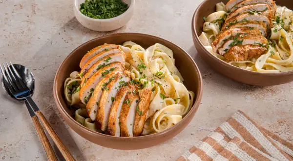 Zwei Schüsseln cremiger Pasta mit geschnittenem Hähnchenbrustfilet, bestreut mit Petersilie. Ein köstliches Chicken Alfredo Rezept für jeden Anlass.