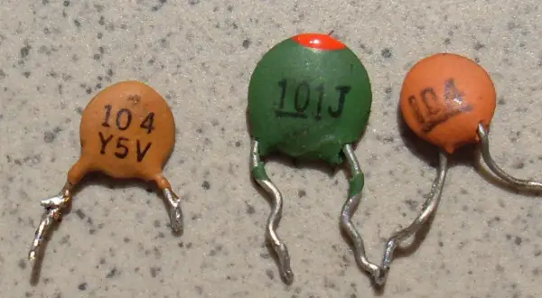 Trzy ceramiczne kondensatory z widocznymi oznaczeniami, np. "104".