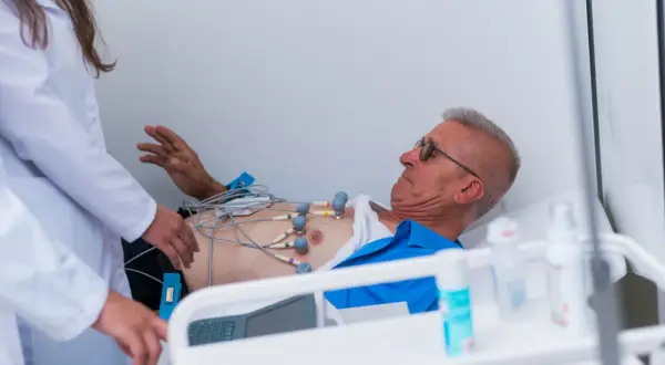 Mężczyzna z elektrodami EKG na klatce piersiowej, pod opieką lekarzy, w stanie przedzawałowym.