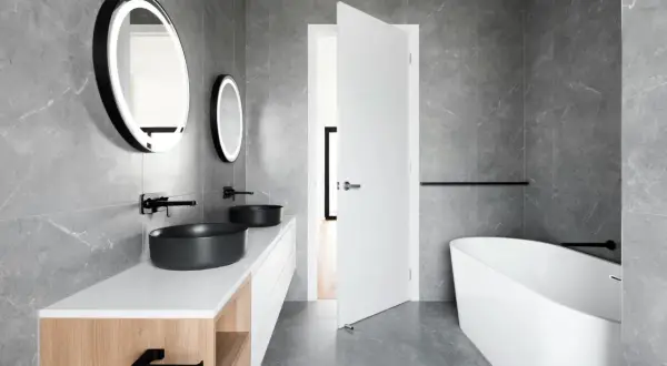 Elegante baño blanco y negro pequeño con lavabos negros, bañera exenta y espejos redondos iluminados.
