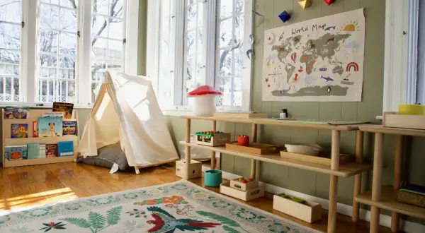 A child's playroom set up with the Montessori method at home, featuring a tent, world map, and wooden shelves with educational toys and books.