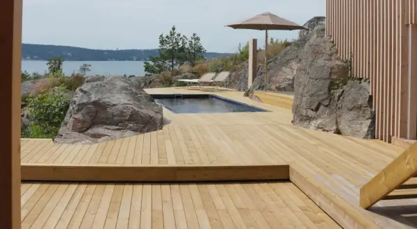 En stor altan i trä med pool och solstolar, omgiven av klippor och med utsikt över havet. Trall mått är perfekt för detta sommarparadis.