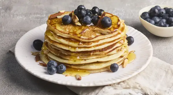 Stapel goldbrauner Pancakes, garniert mit Blaubeeren, Mandelsplittern und Honig. Ein köstliches Rezept für High Protein Pancakes.