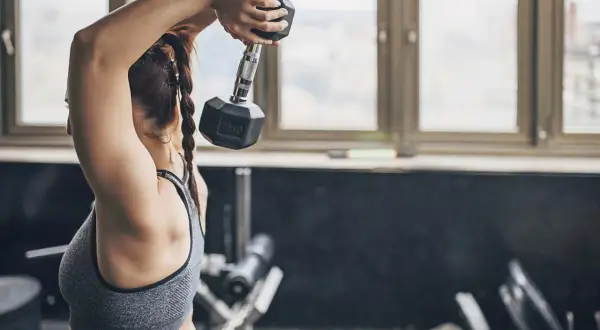 Kvinna utför tricep press med en hantel i gymmet.