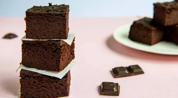 Ciemne, wilgotne brownie z fasoli, ułożone w stosik, obok kawałków czekolady.